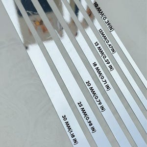 May include: A series of six parallel silver metallic strips arranged diagonally. Each strip is labeled with its width in millimeters and inches: 10 mm (0.39 in), 12 mm (0.47 in), 15 mm (0.59 in), 18 mm (0.71 in), 20 mm (0.79 in), 25 mm (0.98 in), and 30 mm (1.18 in).