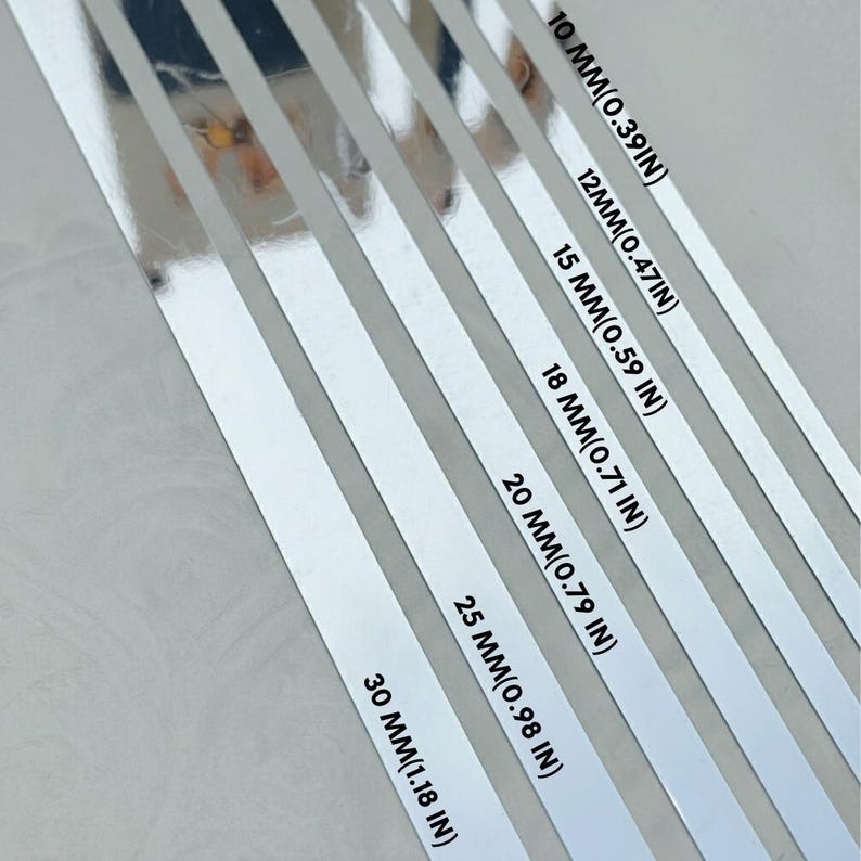 May include: A series of six parallel silver metallic strips arranged diagonally. Each strip is labeled with its width in millimeters and inches: 10 mm (0.39 in), 12 mm (0.47 in), 15 mm (0.59 in), 18 mm (0.71 in), 20 mm (0.79 in), 25 mm (0.98 in), and 30 mm (1.18 in).