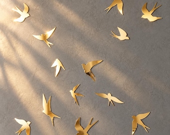 May include: A collection of twelve gold-colored swallow-shaped wall decals arranged in a scattered pattern. Each bird silhouette features a reflective, metallic finish with pointed wings and forked tails, creating a dynamic flying effect.