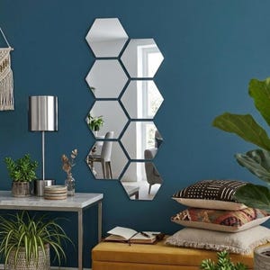 Könnte beinhalten: Sieben sechseckige Spiegel an einer tealblauen Wand. Die Spiegel reflektieren die Raumausstattung, einschließlich Möbeln und Pflanzen. Eine silberne Lampe und Dekorationsartikel stehen auf einem Tisch mit Marmorplatte. Kissen und eine Pflanze sind im Vordergrund.