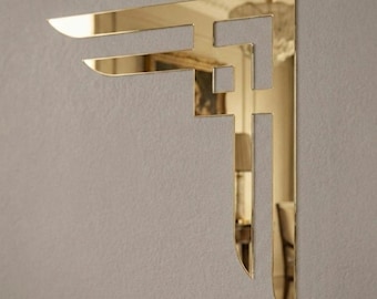 May include: A gold-colored, Art Deco-style wall decor piece. The design features a geometric, angular shape with cut-out sections, creating a layered effect. The reflective surface adds a touch of elegance. The decor is mounted on a neutral-colored wall.