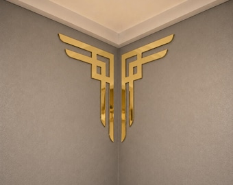 May include: A pair of gold-colored, reflective wall decals featuring a geometric, angular design. Each piece consists of interconnected lines forming a symmetrical corner accent, with a polished, metallic finish that reflects light.