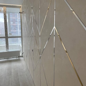 May include: A wall paneling system featuring large, matte beige rectangular panels arranged in a geometric pattern. Thin, reflective silver metal strips are inlaid between the panels, creating a continuous zigzag and diamond design across the surface.