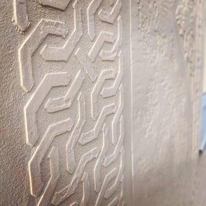 May include: A light beige wall panel featuring a raised, repeating geometric pattern of interlocking angular lines. The surface has a textured, matte finish with a distinct vertical border separating the patterned section from a plain area.