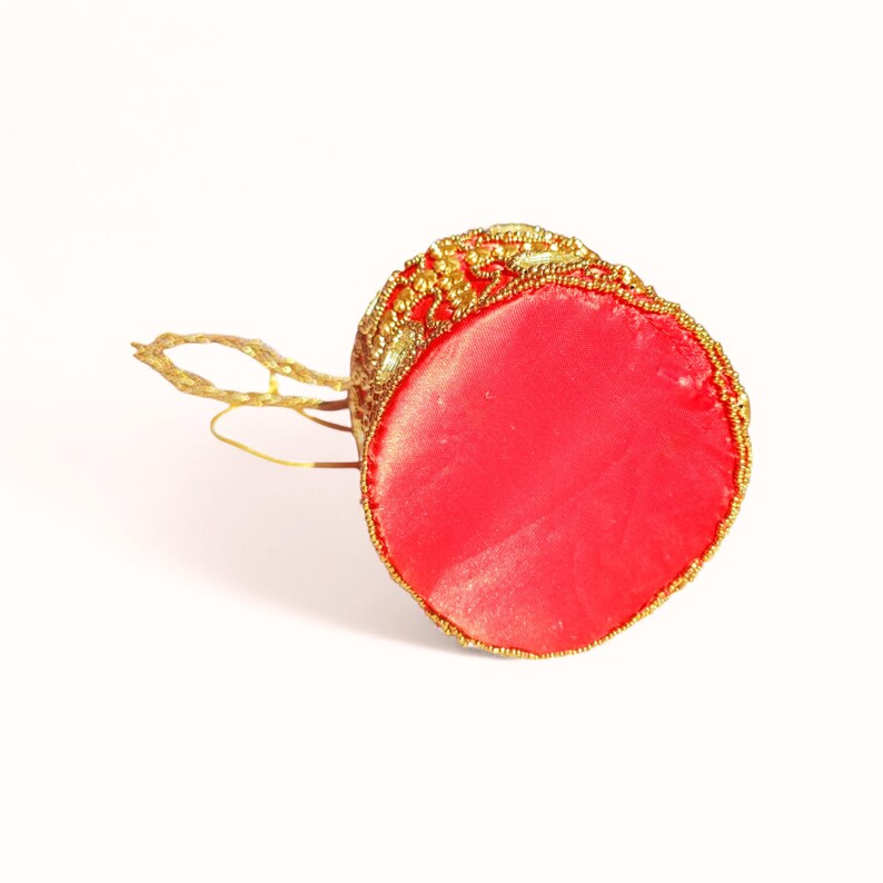 May include: A red and gold beaded ornament with a gold string loop. The ornament has a red satin base and is decorated with gold beads and embellishments. The top of the ornament is a detailed gold design.