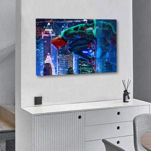 Puede incluir: Una impresi&oacute;n en lienzo que presenta a un superh&eacute;roe con un traje rojo y verde, colgado boca abajo contra un tel&oacute;n de fondo de un paisaje urbano nocturno. Los edificios est&aacute;n iluminados con luces azules y blancas.