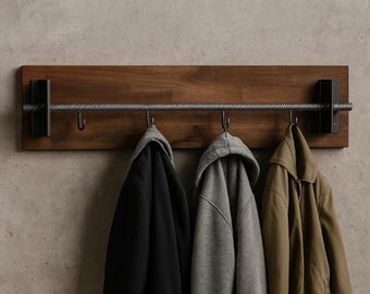 Puede incluir: Un perchero de pared de madera oscura con una barra metálica y ganchos. Cuelgan tres abrigos: negro, gris y verde oliva. El diseño es minimalista e industrial, perfecto para entradas.