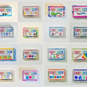May include: A collection of Busy Box educational kits, each in a clear plastic container. The boxes feature colorful labels with various themes, including alphabet, animal matching, and color shape matching. The kits are designed for children.