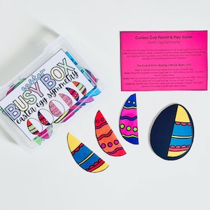 May include: A clear plastic container with a label reading "Easter Busy Box Easter Egg Symmetry" contains colorful egg-shaped cutouts. Several egg halves and a whole egg are displayed, along with a pink guide titled "Curious Cub Parent & Play Guide Easter Egg Symmetry."