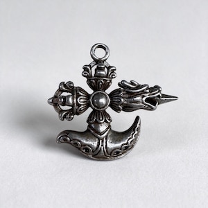 Pode incluir: Um pingente de metal prateado com um núcleo circular central e quatro braços radiantes. Um braço é uma cabeça de dragão estilizada, outro é uma estrutura tipo vajra e a parte inferior é uma forma curva semelhante a uma lâmina com um elo no topo.