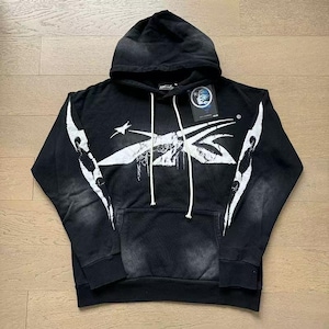 May include: Black hoodie with a white graphic design across the chest and sleeves. The hoodie has a drawstring hood, a kangaroo pocket, and a tag attached. The design includes a star and abstract shapes.