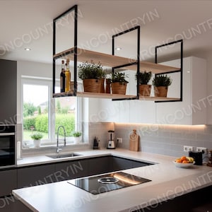 May include: A modern kitchen with a black and wood hanging shelf unit. The shelves hold potted plants and bottles. The kitchen features a white countertop, a built-in cooktop, and a window overlooking a green yard.