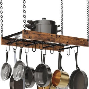 May include: A hanging pot rack with a dark wood and black metal frame. The rack is suspended by chains and holds various pots and pans, including a black pot and several frying pans. The rack has hooks for hanging cookware.