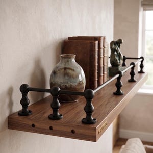 May include: A wall-mounted wooden shelf featuring a dark brown wood grain finish and a black metal railing with decorative posts. The shelf holds a round ceramic vase with blue and brown tones, three leather-bound books, and a small dark sculpture.