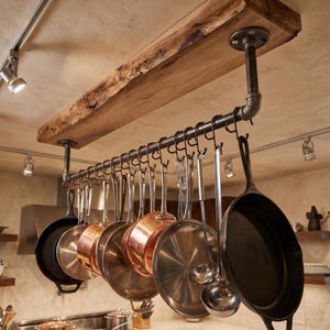 May include: A ceiling-mounted pot rack featuring a natural live-edge wooden beam supported by dark metal industrial pipes. A series of black metal hooks hang from the pipe, holding various copper, stainless steel, and cast iron cookware.
