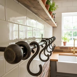 May include: A kitchen scene with a dark metal pot rack and S-hooks. A wooden shelf above holds terracotta plant pots. The wall is tiled with white rectangular tiles, and a brick section adds a rustic touch. The kitchen has a farmhouse style.