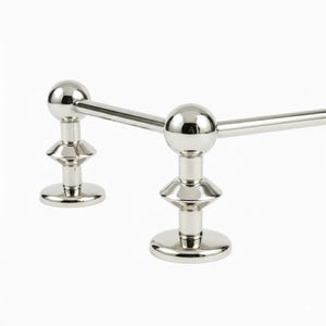 May include: A polished chrome towel bar with a unique design. The bar features two spherical finials connected by a horizontal bar. The finials are supported by decorative, tiered bases, creating a modern and elegant look.