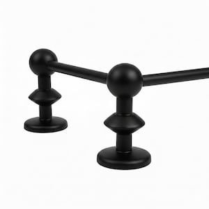 Puede incluir: Una barra de toalla negra mate con un diseño minimalista. La barra presenta dos soportes de extremo redondeados con una base escalonada y una parte superior esférica. La barra horizontal conecta los soportes, creando un aspecto elegante y moderno para un baño.