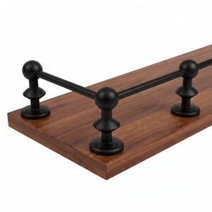 May include: A rectangular wooden shelf with a rich brown wood grain finish, featuring a matte black metal railing attached to the top surface. The railing consists of three vertical posts with spherical finials connected by horizontal metal bars.