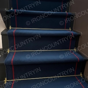 May include: A set of navy blue stair runners with a thin red stripe down the center. The runners are secured with brass rods and brackets. The stairs are made of dark wood.