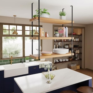 Może przedstawiać: Nowoczesna kuchnia z białą wyspą z blatem i granatowymi szafkami. Biały zlew gospodarczy ustawiony jest na zielonej płytce backsplash. Wisząca drewniana półka eksponuje rośliny, naczynia i artykuły kuchenne. Złote lampy wiszące nad zlewem.