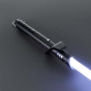 Op de afbeelding: Een zwart lichtzwaard met een wit zwaard. De handgreep heeft een getextureerde grip, een zilveren knop en een zwarte clip. Het lichtzwaard staat tegen een donkergrijze achtergrond.