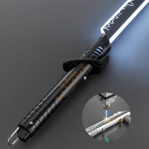 Op de afbeelding: Zwart lichtzwaard met een helder wit blad. De handgreep is gegraveerd met de tekst "To Lucius, May the Force Be With You." Een kleinere afbeelding toont het graveerproces op een zilveren lichtzwaard.