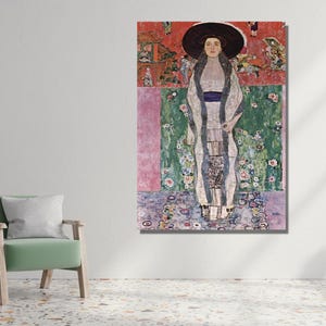 May include: A framed print of a Gustav Klimt painting. The artwork depicts a woman in a long, patterned dress and a large hat. The background features floral and geometric patterns in shades of red, green, and purple.