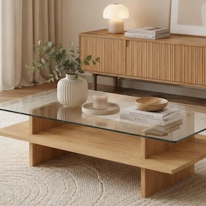 Può includere: Un salotto moderno con un tavolino rettangolare in legno e vetro. Il tavolo presenta libri, una piccola ciotola e una candela. Un tappeto chiaro e un mobile in legno completano l'arredamento.