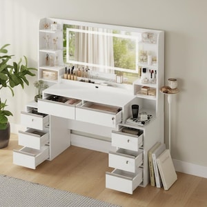 May include: A white vanity desk with a built-in lighted mirror and multiple drawers. The desk has a clean, modern design with open shelves and a small side table. A potted plant and books are visible in the background.