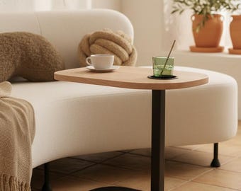 Mesa auxiliar en forma de C con altura regulable, tablero de madera clara y base de metal negro para salón.