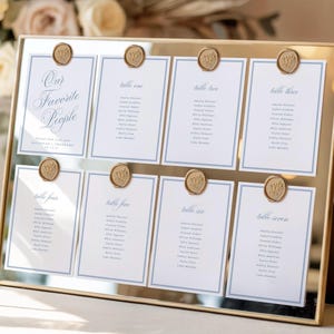May include: A gold-framed mirror seating chart featuring eight white cards with blue borders and text. The cards are secured with gold wax seals. The top left card reads Our Favorite People, while the others list table numbers one through seven.