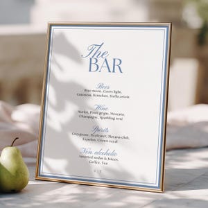 May include: A vertical rectangular sign in a thin gold frame featuring the text The BAR in blue, followed by lists for Beer, Wine, Spirits, and Non alcoholic beverages with specific drink names, all printed on a white background with a blue border.