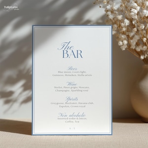 May include: A rectangular menu card with a blue border and text that reads "The Bar." The menu lists beer, wine, spirits, and non-alcoholic beverages. The card is on a white background with a floral arrangement in the background.