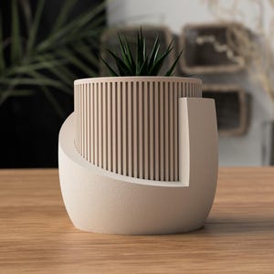 May include: A modern, beige-colored planter with a cylindrical, slatted upper section and a curved base. The planter holds a small, green succulent. The design is minimalist and contemporary, suitable for indoor decor.