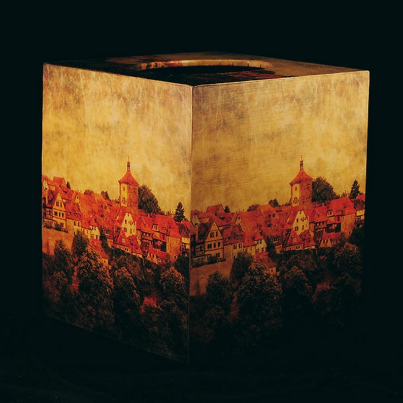 May include: A square wooden box with a vintage-style image of a European town with red-tiled roofs and a church steeple. The box has a distressed, aged look with a light brown background.
