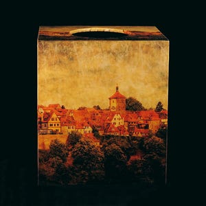 May include: A wooden tissue box cover with a vintage-style image of a European town with red-tiled roofs and a tall tower. The image has a faded, antique look.