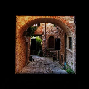 May include: A narrow, cobblestone alleyway in a historic Italian village. The alleyway is lined with brick buildings with arched doorways and windows. The buildings are painted in shades of yellow, orange, and brown.