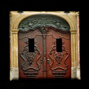 May include: A double door with intricate carvings and a decorative archway above. The door is made of dark wood and has a reddish-brown finish. The archway is made of a light-colored stone and has a yellow-gold finish.