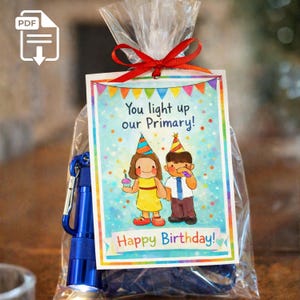 May include: A gift bag with a red ribbon, containing a blue flashlight and a card. The card reads "You light up our Primary!" and "Happy Birthday!" with cartoon illustrations of children wearing party hats.