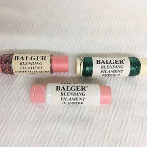 May include: Three spools of Balger Blending Filament in Confetti Fuschia, Emerald, and Hi Luster White. Each spool is wrapped in a pink paper with the brand name and color printed on the label. The spools are on a white textured surface.