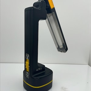 May include: A black and yellow portable work light with a fluorescent tube. The light has a rectangular base and a handle. The top section has an orange lens. The light has a yellow switch and a yellow stripe around the base.
