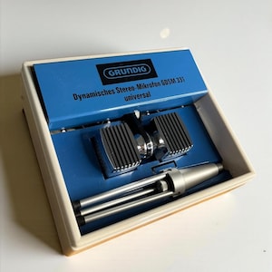 May include: Vintage Grundig stereo microphone set in its original box. The box is blue and cream-coloured, with the Grundig logo and product information printed on the lid. The set includes two microphones and a small silver stand.