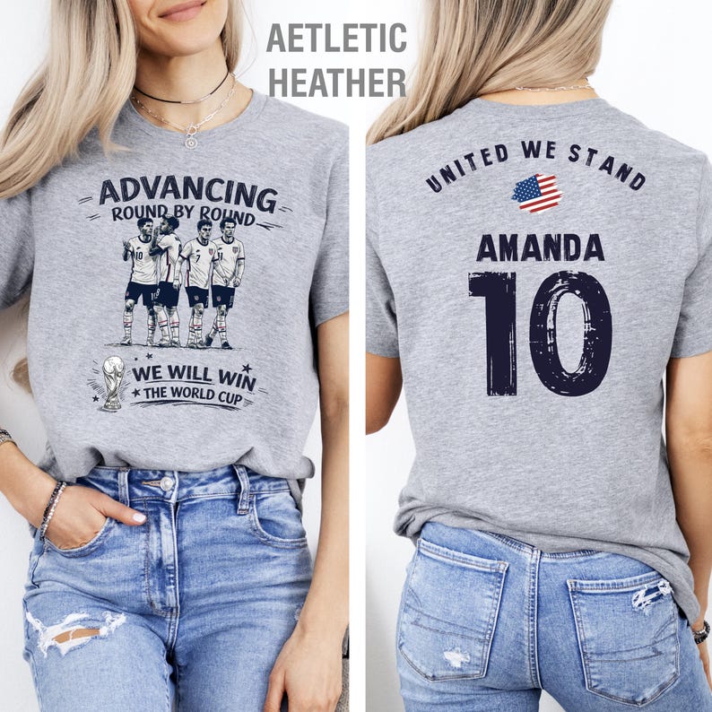 May include: Athletic heather gray t-shirt with a soccer-themed design. The front features a team graphic and the text "ADVANCING ROUND BY ROUND" and "WE WILL WIN THE WORLD CUP". The back displays "UNITED WE STAND", the name "AMANDA", and the number "10".