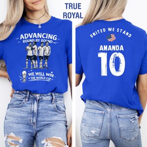 May include: Royal blue t-shirt with the text "ADVANCING ROUND BY ROUND" and "WE WILL WIN THE WORLD CUP". The back of the shirt has "UNITED WE STAND", the name "AMANDA", and the number "10".
