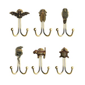 May include: A set of six antique brass-toned metal wall hooks, each featuring a unique animal or insect figure at the top, including a bat, cicada, owl, snake, dog, and turtle, all mounted on double-pronged hooks with rounded ball ends.