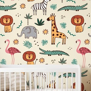 Könnte beinhalten: Ein Kinderzimmer mit cremefarbenen Tapeten mit einem Muster aus Zeichentieren: Giraffen, Löwen, Elefanten, Flamingos, Zebras und Krokodilen. Ein weißes Kinderbett und eine Holzkommode befinden sich im Vordergrund.