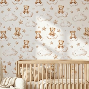 Könnte beinhalten: Ein Kinderzimmer mit einem hellen Holzbett, einer Kommode und einem Schaukelstuhl. Die Tapete zeigt ein sich wiederholendes Muster aus Teddybären, Wolken und Sternen in Braun- und Beigetönen. Ein runder Teppich und Regale mit Dekoration vervollständigen den Raum.