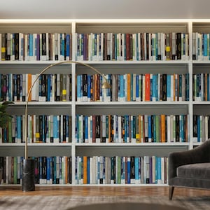 Könnte beinhalten: Ein Bibliotheksinterieur mit einer Stehlampe, einer Topfpflanze und einem dunkelgrauen Sessel. Die Regale sind mit Büchern in verschiedenen Farben gefüllt, was eine warme und einladende Atmosphäre schafft.