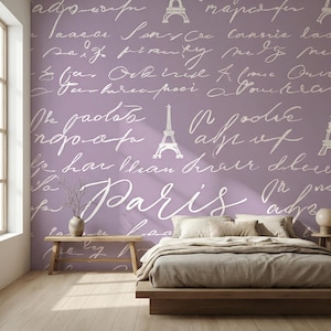 Könnte beinhalten: Schlafzimmer mit einer lavendelfarbenen Wand, die mit weißer Schrift und Eiffelturm-Illustrationen verziert ist. Das Wort "Paris" ist deutlich sichtbar. Eine Holzbank und ein Bettrahmen ergänzen die Einrichtung.